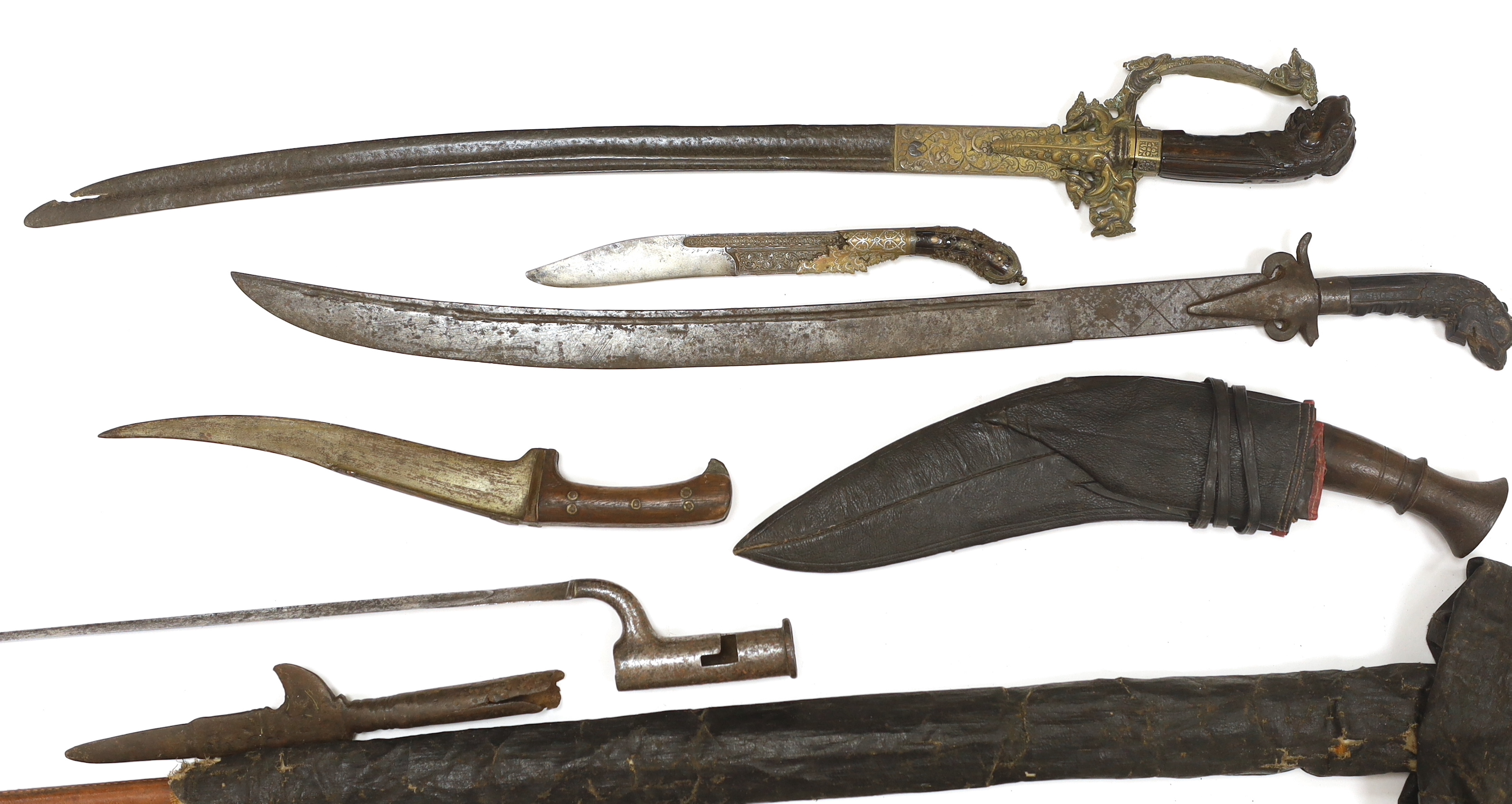 Two Sinhalese daggers and a kukri, a silver inlaid Kirichchiya dagger, together with another in a scabbard with a long pin, another dagger with a wooden handle, a head of a brass inlaid iron pole arm, a George V 1897 pat